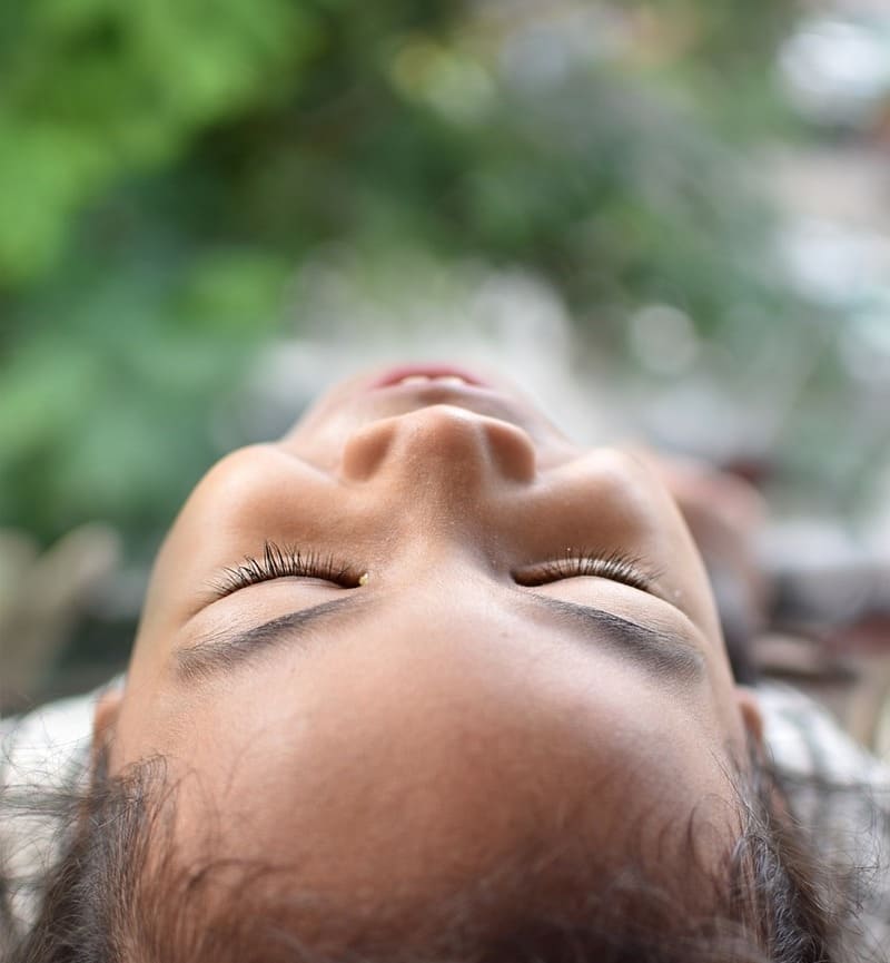 Zoom sur le visage souriant d'une enfant allongée au sol, les yeux fermés et le visage tourné vers le ciel. Elle semble apaisée et sereine, symbolisant les bienfaits de la sophrologie pour les enfants.
