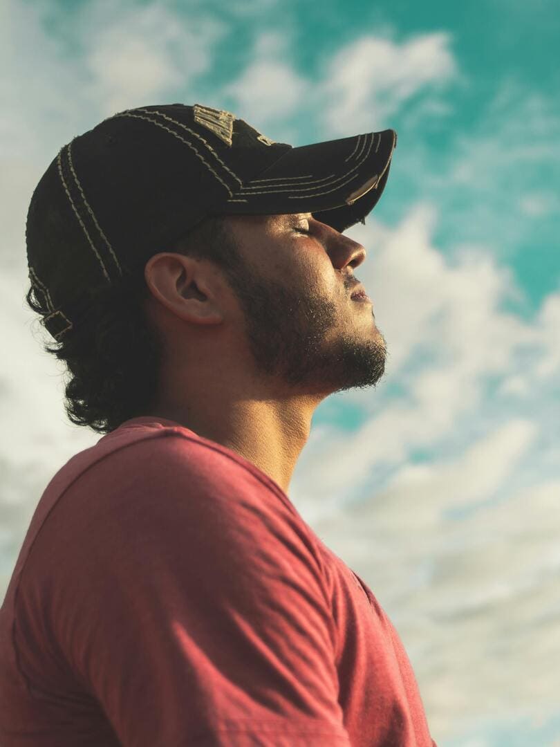 Portrait d'un homme de profil, yeux clos, inspirant sereinement sous un ciel bleu. Corps orienté vers l'avenir, évoquant plénitude, apaisement, calme, harmonie et légèreté