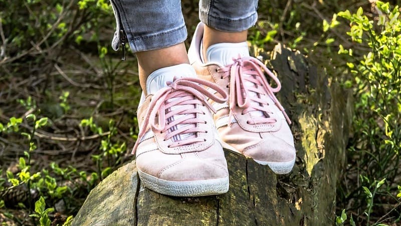 Focalisation sur des pieds chaussés de baskets roses avançant en équilibre sur un tronc d'arbre dans une forêt, symbolisant la progression, l'équilibre et la confiance en soi