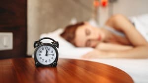 Réveil indiquant la nuit avec en arrière-plan la silhouette d'une personne endormie, symbolisant les ateliers sur le sommeil et la gestion des troubles nocturnes grâce à la sophrologie
